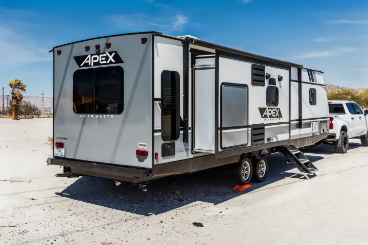 A grey Apex Ultralite travel trailer rv rental is set up in a sunny, dry outdoor location with a white pickup.. Coachmen Apex 2021