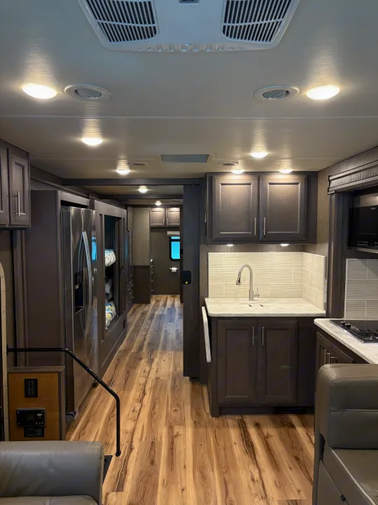 Spacious RV rental interior with full kitchen, living area, and hallway leading to bunks. Features dark cabinetry, wood-look floors, and ample lighting.. Thor Challenger 2021