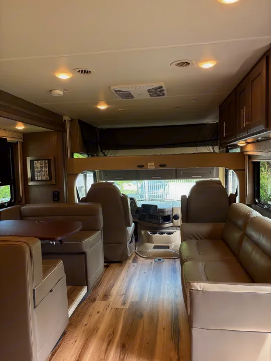 Spacious RV rental interior, featuring a modern dinette, sofa, driver's cabin, and convenient overhead bunk.. Thor Challenger 2021