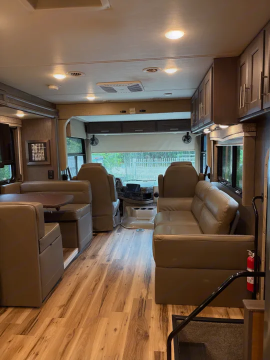 Inside a comfortable RV rental: light wood flooring, a dinette, sofa seating, and the driver's area up front.. Thor Challenger 2021