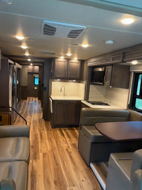 Inside a sleek rv rental: kitchen with sink & stove, dinette, cozy sofa, and realistic wood flooring in a neutral palette.. Thor Challenger 2021