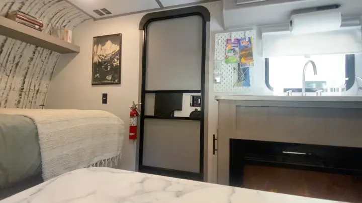 Cozy RV rental interior featuring a bed, kitchen sink, fireplace, and an exit door, offering a compact living space.. Coleman 17B 2024