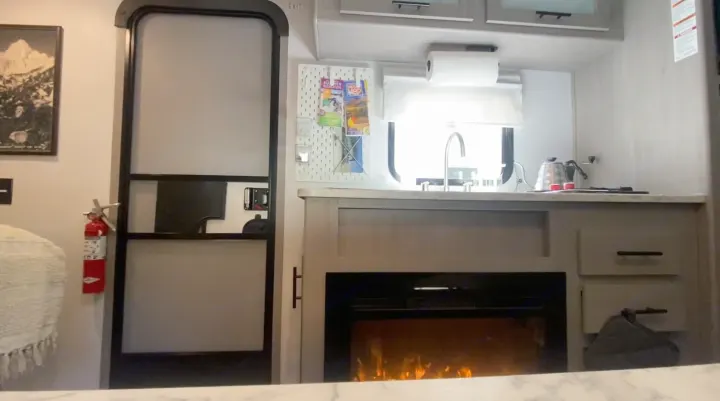 RV rental: Compact interior showing kitchen, sink, fireplace with flames, and a fire extinguisher for safety.. Coleman 17B 2024