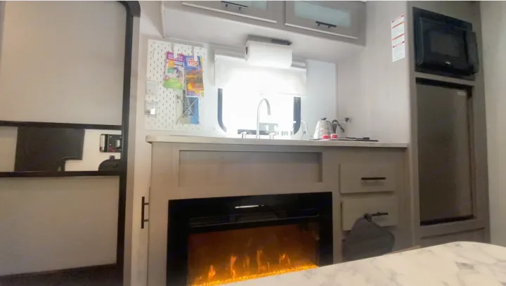 Explore this RV rental's modern interior: compact kitchen, microwave, fridge, and an inviting electric fireplace.. Coleman 17B 2024