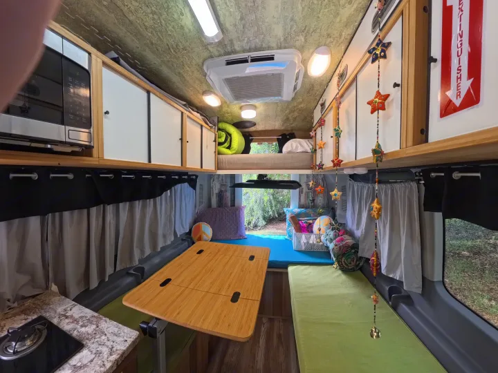Inside this RV rental: functional kitchen with microwave, convertible dining/lounge area with table, and a compact bunk bed.. Ford Transit Custom 2015
