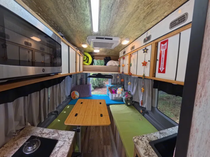 Colorful RV rental interior showcasing kitchen, dining, seating, and overhead bunk for travel.. Ford Transit Custom 2015