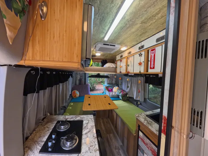 Cozy rv rental interior with kitchen, dining area, and bunk beds, offering a glimpse of nature outside.. Ford Transit Custom 2015