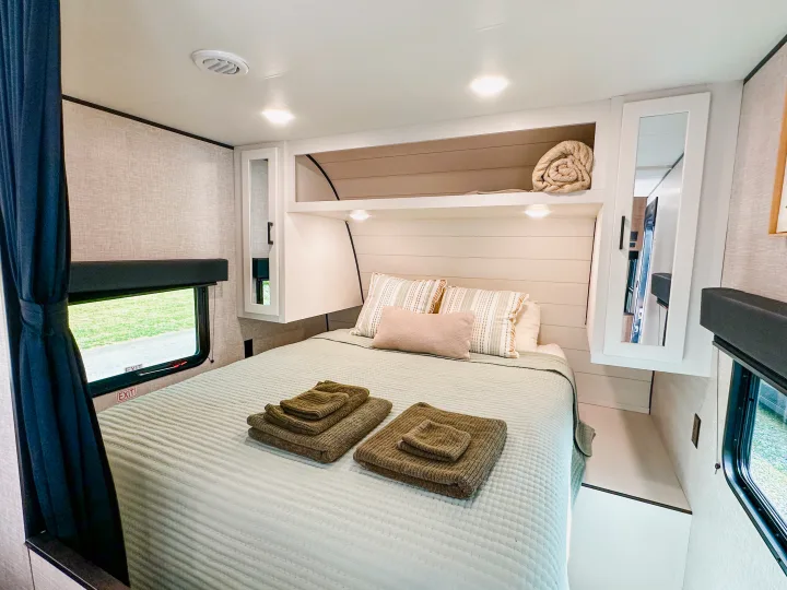 Cozy RV rental bedroom showing a bed with light green quilted bedding, folded brown towels, mirrored cabinets, and overhead storage.. Jayco Jay Flight SLX 2024