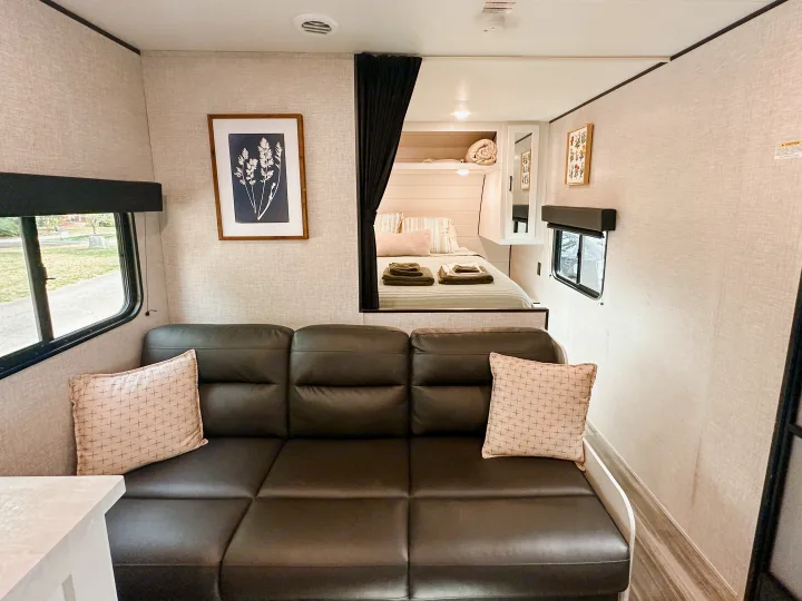 Bright and modern RV rental living space featuring a sofa, wall art, and a glimpse into the cozy bedroom through a curtain.. Jayco Jay Flight SLX 2024