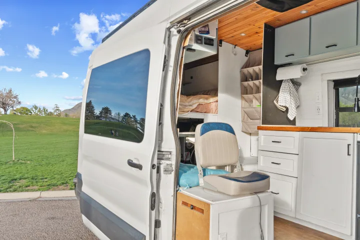RV rental: A white camper van with its side door open, revealing a cozy converted interior, bed, kitchen, and storage.. Ford Van 2015