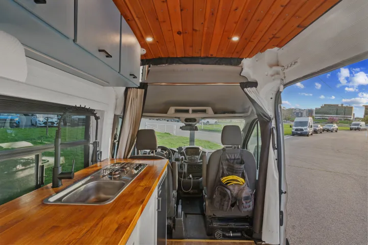 RV rental interior showing a custom kitchen with a sink/stove, wooden ceiling, and driver's cab.. Ford Van 2015