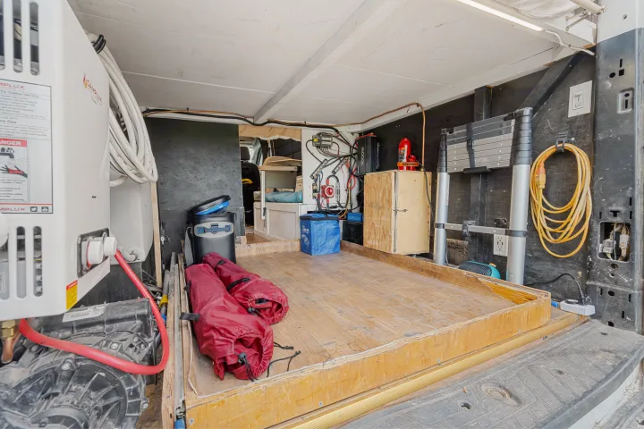 This RV rental interior shows a custom camper van setup with a water heater, electrical, storage, and a bed area for adventure.. Ford Van 2015