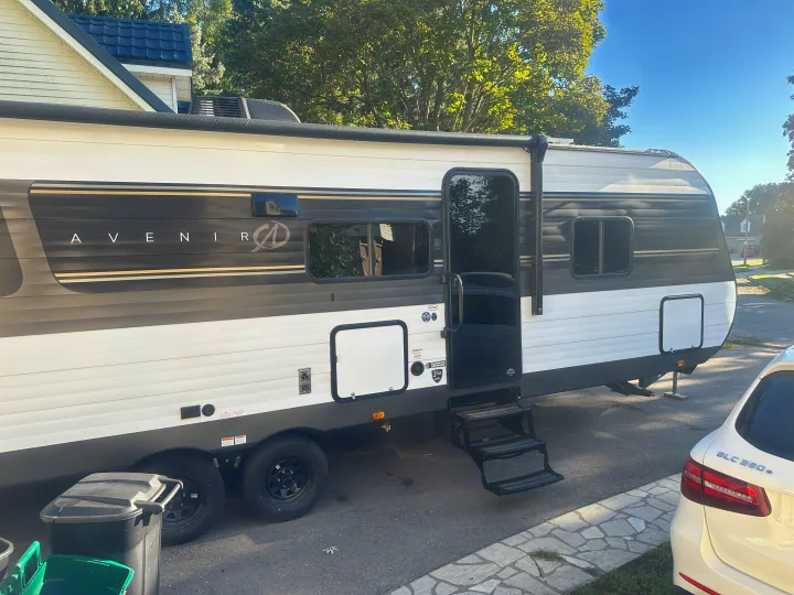 Exterior side view of a white and dark grey Avenir travel trailer, an RV rental, with steps extended and multiple windows visible.. Cruiser RV Avenir 2024