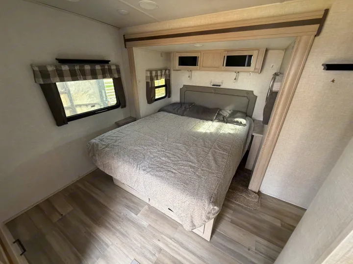 Bright RV rental bedroom with a gray bed, windows, overhead cabinets, and wood-look flooring, ideal for travel.. Forest River Flagstaff Super Lite 2021