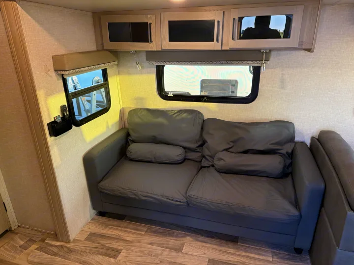 Cozy RV rental living area featuring a grey sofa, upper storage cabinets, and side windows.. Forest River Flagstaff Super Lite 2021