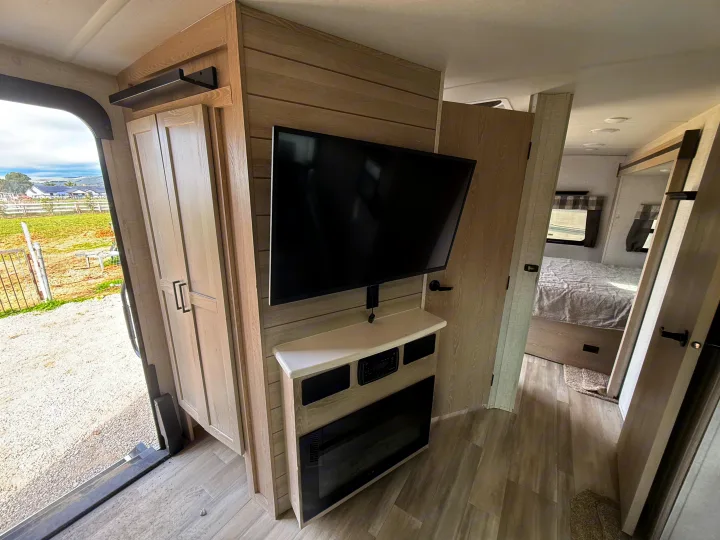 Modern rv rental interior: living area with TV, electric fireplace, wardrobe, and views into the bedroom and outdoors.. Forest River Flagstaff Super Lite 2021