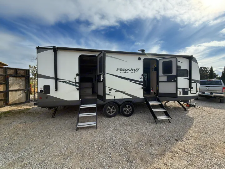 White Flagstaff Super Lite travel trailer RV rental parked on gravel with open doors, stairs, & extended slide-out.. Forest River Flagstaff Super Lite 2021