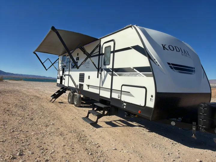 A Kodiak Ultra Lite travel trailer rv rental with an extended awning, parked by a desert lake on a sunny day.. Dutchmen Kodiak Ultra Lite 2021