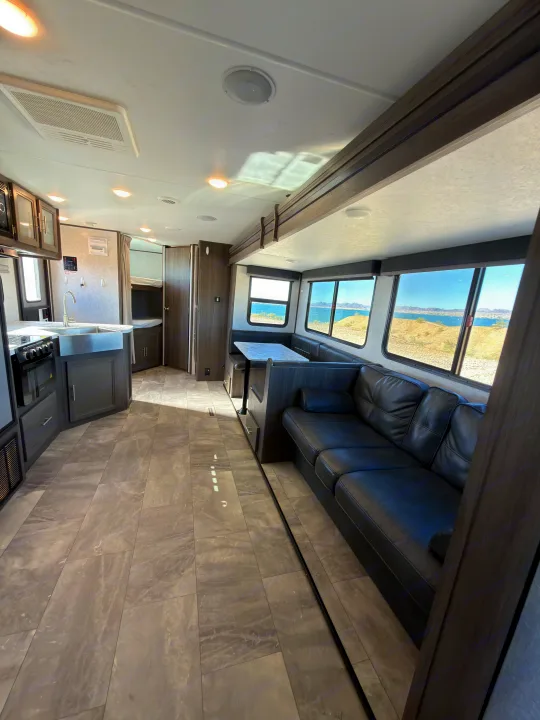 Modern RV rental interior featuring a kitchen, dinette, black sofa, and bunk beds, with scenic lake and mountain views. Perfect for travel.. Dutchmen Kodiak Ultra Lite 2021
