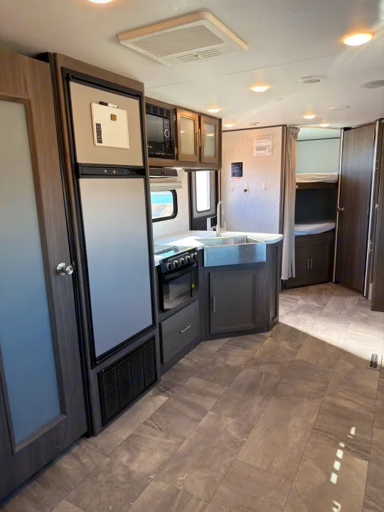 Well-equipped rv rental interior. Modern kitchen with fridge, stove, sink, and microwave. Bunk beds are visible in the back.. Dutchmen Kodiak Ultra Lite 2021