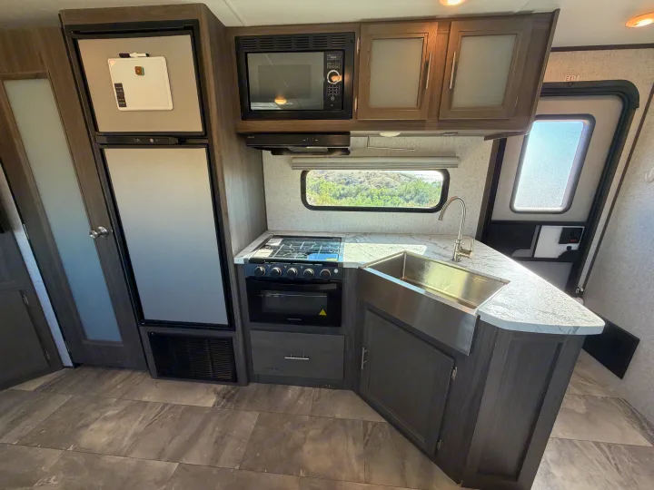 This RV rental kitchen features a full-size fridge, microwave, stove, oven, sink, and ample cabinets.. Dutchmen Kodiak Ultra Lite 2021