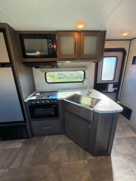 Explore this RV rental's modern kitchen, featuring a microwave, stove, farmhouse sink, and storage cabinets, with a window view.. Dutchmen Kodiak Ultra Lite 2021