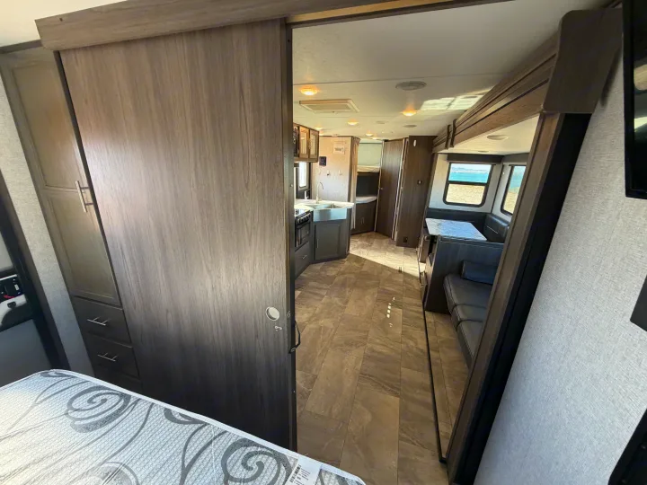 Modern rv rental interior: kitchen, dining booth, and bedroom area with a glimpse of ocean through windows. Tiled floor.. Dutchmen Kodiak Ultra Lite 2021
