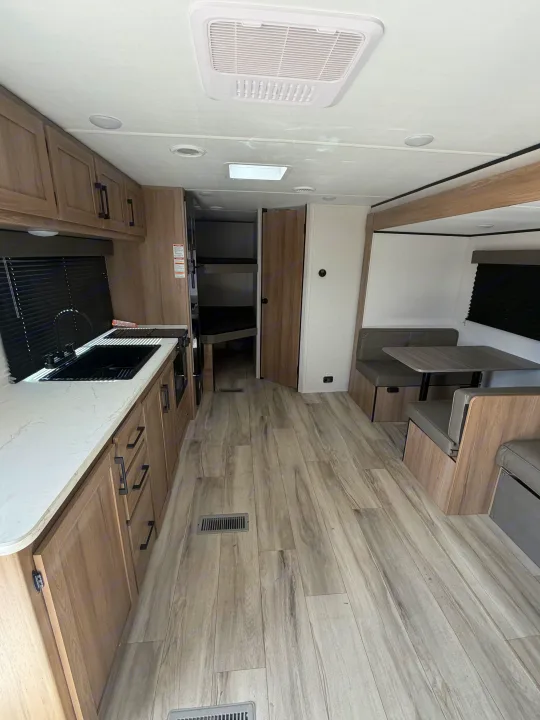 Modern RV rental interior featuring a well-equipped kitchen, dinette, and cozy bunk beds in light wood and gray tones.. Keystone Coleman 2026
