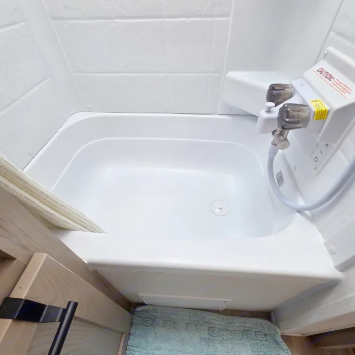 Inside an RV rental: a pristine white shower and small bathtub, complete with fixtures, drain, and shower curtain.. Forest River Rockwood Geo Pro 2024