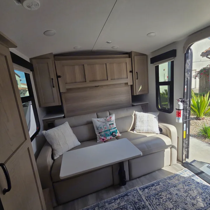 Bright rv rental living space with a pull-down sofa bed, adjustable table, wooden cabinets, and modern amenities.. Forest River Rockwood Geo Pro 2024