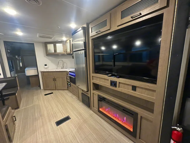 Modern RV rental interior showing a kitchen, entertainment center with TV & fireplace, and dining booth.. Keystone RV Hideout Luxury 2021
