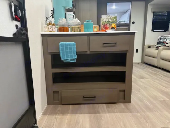 An rv rental's sleek kitchen island with a coffee station, open shelves, and a cozy living space beyond.. Grand Design Transcend 2025