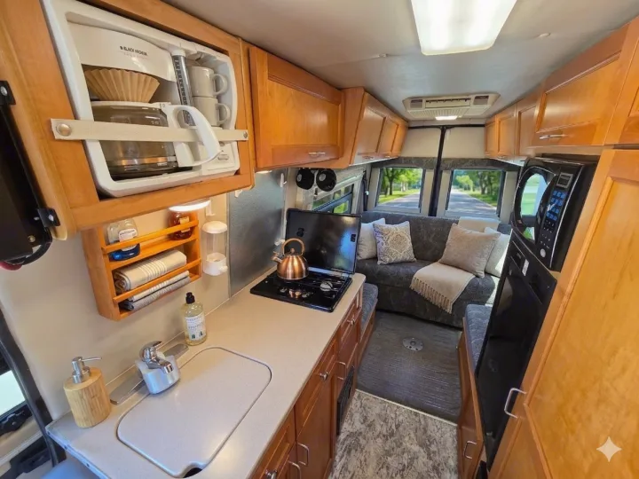 This cozy RV rental interior features a compact kitchen with a stove, sink, and coffee maker, plus a comfortable living area.. Leisure Travel Vans Leisure Travel Vans Class B 2005
