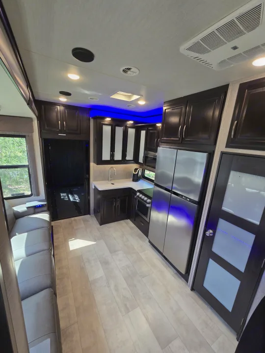This spacious RV rental features a modern kitchen with stainless appliances, dark cabinets, blue lighting, and a comfy gray sofa.. Grand Design Momentum 2019