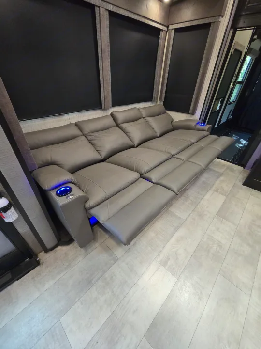 Luxury RV rental interior with grey reclining sofa, blue LED cup holders, and extended footrests. Comfort for your road trip.. Grand Design Momentum 2019