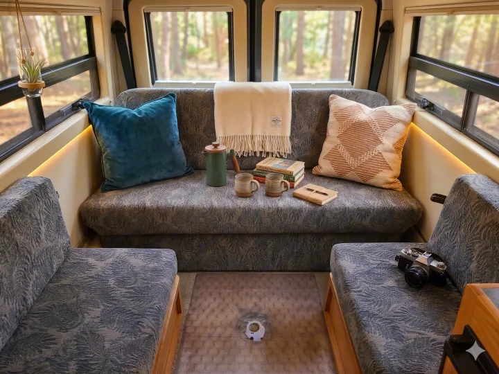 An inviting RV rental interior, featuring soft seating, books, coffee, and an air plant with a forest view.. Leisure Travel Vans Leisure Travel Vans Class B 2005