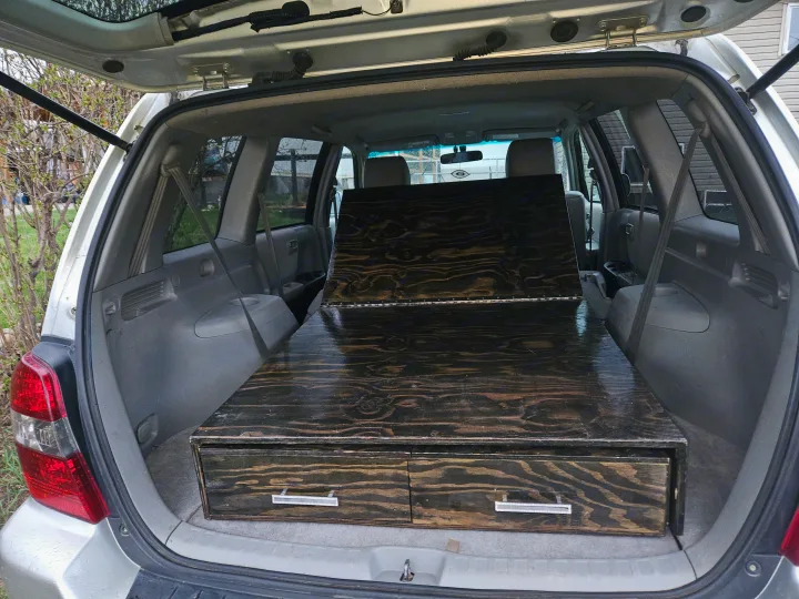 Silver SUV's trunk features a dark wood sleeping platform with storage drawers, ready for car camping or an RV rental trip.. Toyota Highlander 2004