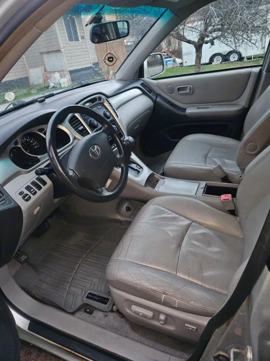 Detailed Toyota car interior with worn leather seats, dashboard, and WeatherTech mats. An RV is outside, possibly for an rv rental adventure.. Toyota Highlander 2004