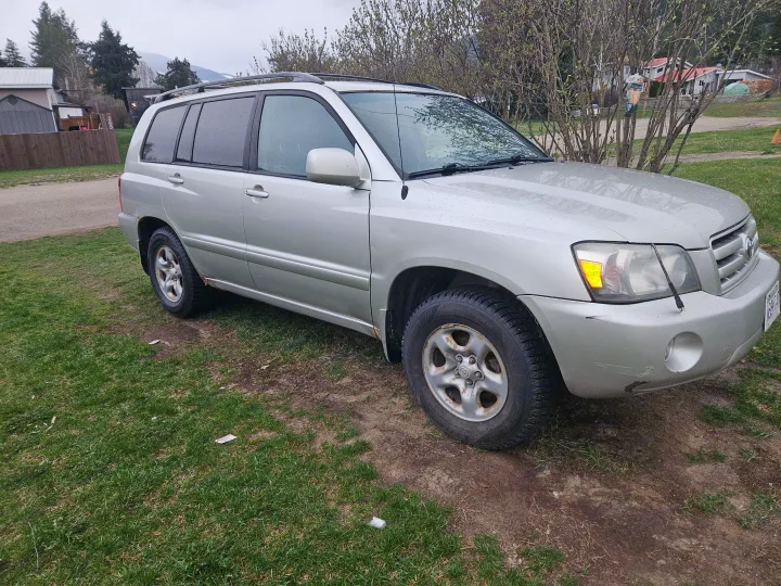 A silver Toyota Highlander SUV, not an RV rental, parked on a grassy area in a rural setting under cloudy skies.. Toyota Highlander 2004