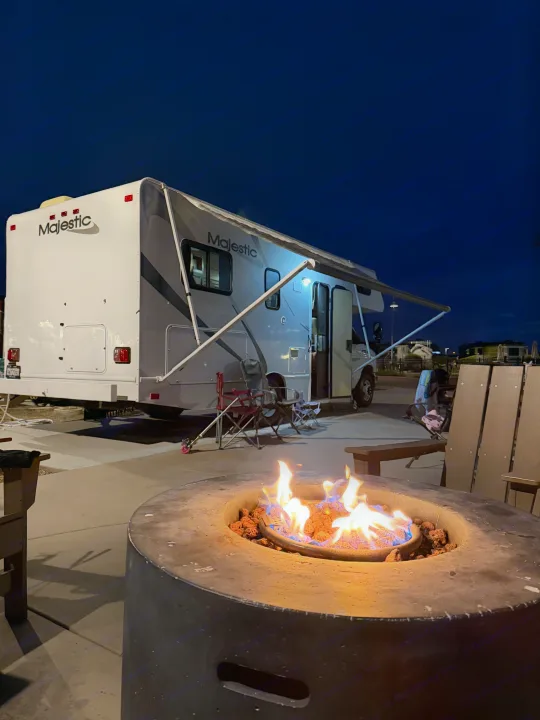 A warm fire pit glows at night, complementing a parked rv rental with its awning out, offering a cozy campsite scene.. Thor Majestic 2013