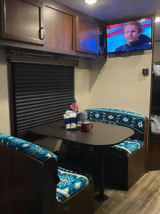 RV rental dinette features comfy blue cushions, a table with a flag & mug, and TV entertainment.. Jayco Jay Flight SLX 2018