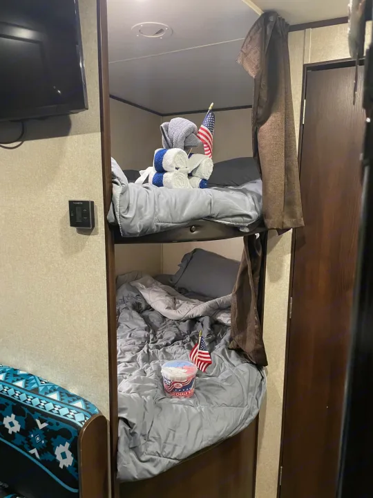Inside an RV rental: two bunk beds with gray bedding, an American flag on each, and decorative towels on the top bunk.. Jayco Jay Flight SLX 2018