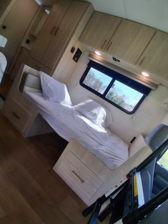 Cozy bunk bed area in an RV rental, featuring light wood cabinets, an access ladder, and a window with a scenic view.. East to West Entrada 2026