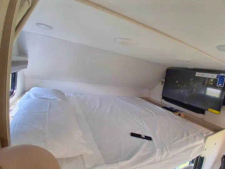 Comfortable RV rental sleeping area with TV, showing a neatly made bed and remote.. East to West Entrada 2026