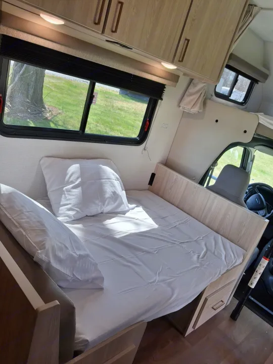 Experience comfort in this RV rental! Features a neatly made bed, bright windows, overhead cabinets, and clever storage solutions.. East to West Entrada 2026