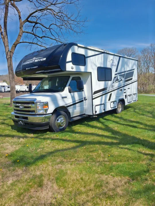 This white and black Forest River Class C RV rental, an Entrada model, is parked on grass under a clear sky, ready for adventure.. East to West Entrada 2026