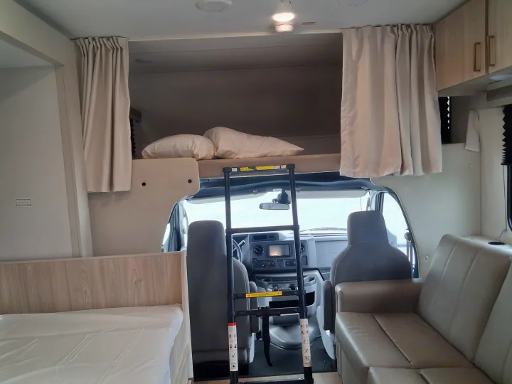 This rv rental's interior features a cab-over bunk with ladder, driver's cockpit, and living area with bed and couch.. East to West Entrada 2027