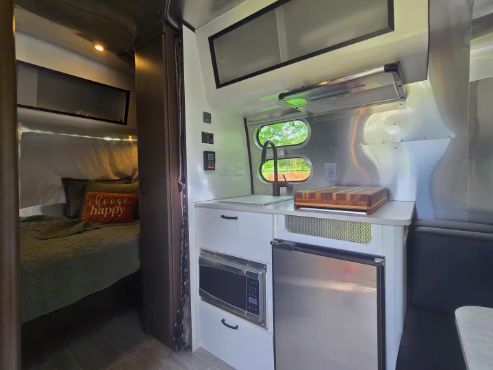 This modern rv rental features a cozy bedroom and a well-equipped kitchen with a microwave, fridge, and sink.. Airstream Caraval 2021