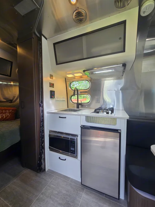 Modern RV rental kitchen with sink, stove, microwave, fridge, and a peek into the cozy bedroom.. Airstream Caraval 2021