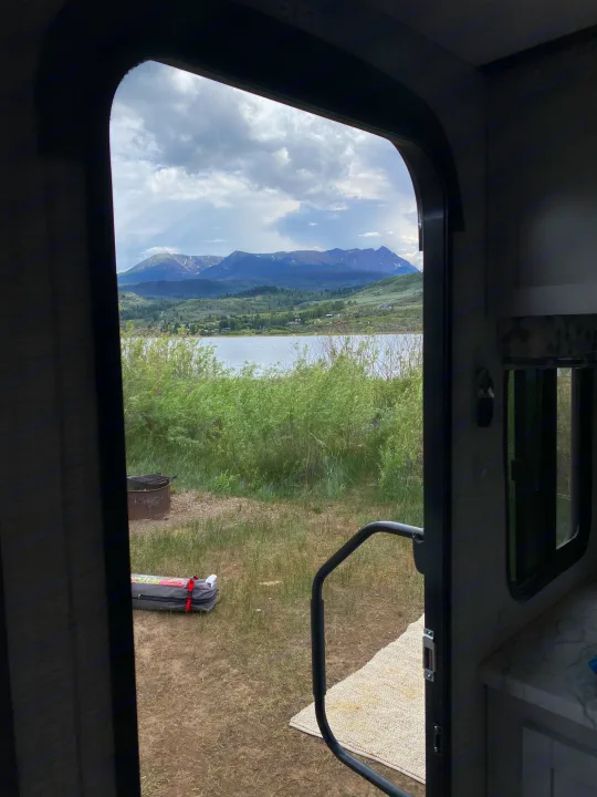 View from an RV rental door: serene lake, majestic mountains, and a fire pit. An ideal scenic camping spot.. Keystone RV Bullet Crossfire 2021